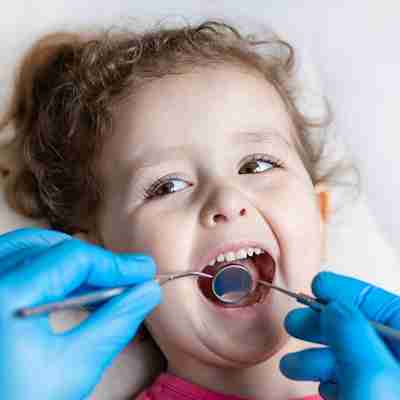 Pediatric Dentistry pediatric dentistry being showcased with a child holding her mouth open as Dr. Michael Koumas DDS PC inserts dental instruments in her mouth with blue gloves on