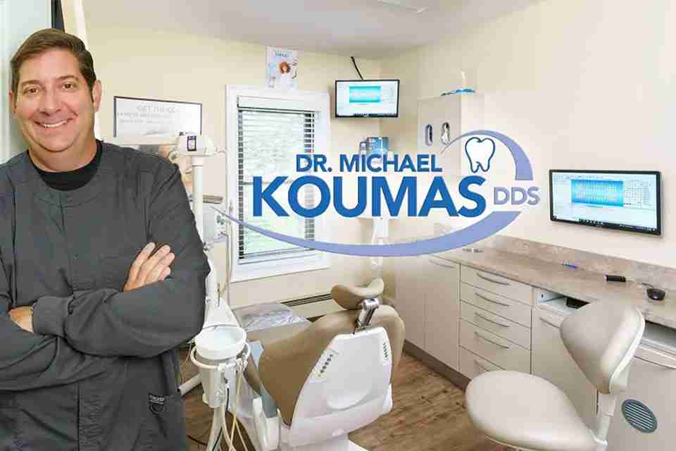 Dr. Michael Koumas DDS PC standing next to his logo in one of his operatories signifying he is a dentist in newburgh ny who has been serving the Hudson Valley for over 23 years